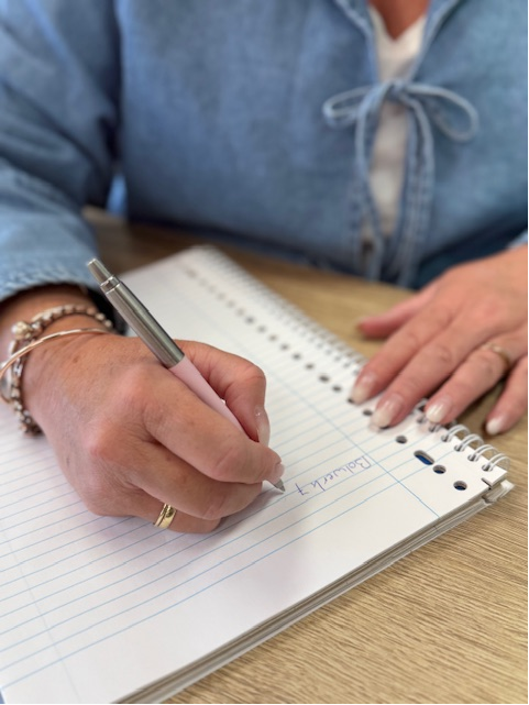 Persoon schrijft in notitieboek met pen op tafel.